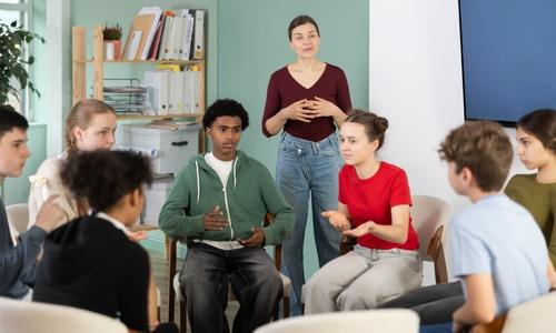 Collaborative,Teenage,Students,Sitting,In,Circle,And,Talking,Under,Supervision